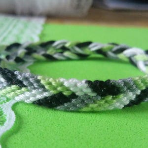 Könnte beinhalten: Ein geflochtenes Freundschaftsarmband mit schwarzen, weißen, grünen und grauen Fäden.