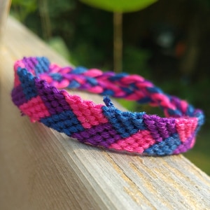 Peut inclure: Un bracelet d'amitié avec un motif en chevron rose, violet et bleu.