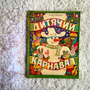 May include: A vintage children's book with a colorful illustration of a snowman and various animal characters. The book cover features the title "ДИТЯЧИЙ КАРНАВАЛ" in bold, decorative lettering, with the author's name above. The cover has a green border.