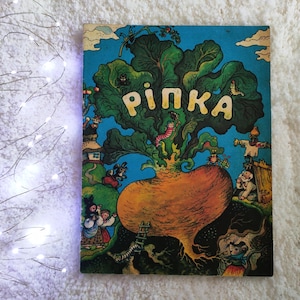 Pode incluir: Uma capa de livro infantil retangular com fundo azul apresentando um grande nabo laranja no centro. O texto "РІПКА" está impresso em letras amarelas acima do nabo. A ilustração inclui vários pequenos animais, um espantalho e pessoas.