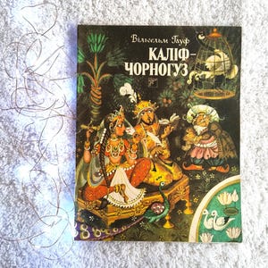May include: A vintage book cover with the title "Каліф-Чорногуз" in Ukrainian. The cover features a colorful illustration of figures in ornate clothing, a bird in a cage, and a peacock. The background is a dark green with floral and tree elements.