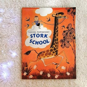 Op de afbeelding: Een vintage kinderboek getiteld "Stork School" met een oranje omslag. De omslag toont een giraffe met een jongen op een wolk en de titel in grote blauwe letters. Het boek heeft een grillige illustratiestijl.