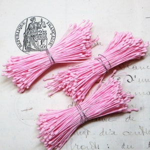May include: Three bundles of pink flower stamens, each tied with a silver wire. The stamens are arranged in a fan shape and are on a white surface.