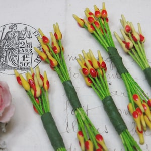 May include: Several bundles of artificial flowers with yellow and red tips and green stems. The stems are wrapped in green tape. The flowers are arranged on a vintage paper background.