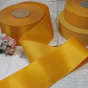May include: A spool of bright yellow satin ribbon. The ribbon is rolled up and has a smooth, shiny finish.