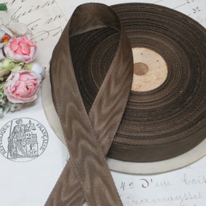 May include: A spool of brown satin ribbon with a textured finish. The ribbon is approximately 1 inch wide and is wound around a cardboard spool.