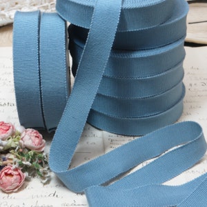 May include: A stack of blue grosgrain ribbon, a type of woven ribbon with a textured surface. The ribbon is arranged in a pile, with the ends of the ribbon extending out from the pile.