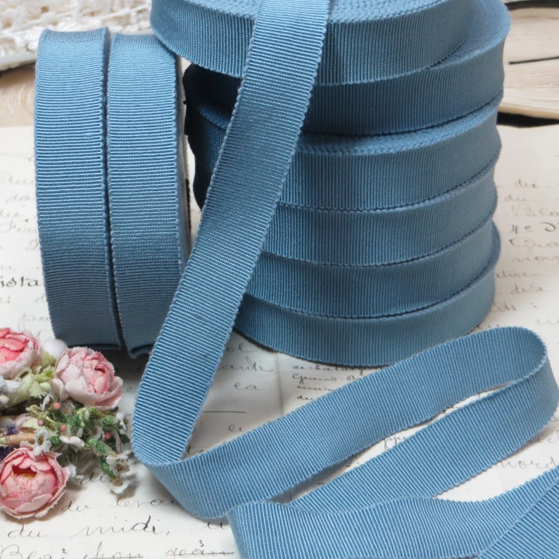 May include: A stack of blue grosgrain ribbon, a type of woven ribbon with a textured surface. The ribbon is arranged in a pile, with the ends of the ribbon extending out from the pile.