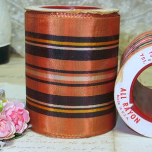 May include: A spool of orange, black, white, and gold striped ribbon. The label reads "All Rayon Made in U.S.A."