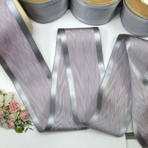 May include: A roll of silver and light purple ribbon with a satin finish. The ribbon has a wide, silver stripe down the center.