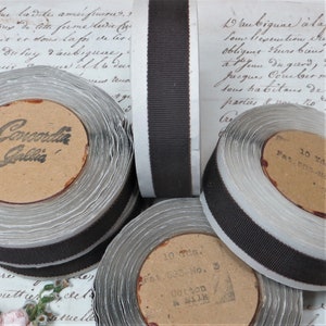 May include: Close-up of spools of brown grosgrain ribbon with white backing. The spools are labelled with "Concordia Gallia" and "Pat. 583-No. 3 Cotton & Silk".