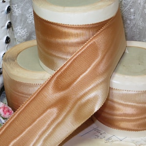 May include: Three spools of gold-colored ribbon with a ribbed texture. The ribbon is wound around cardboard spools.