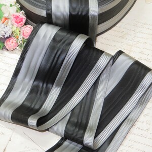 May include: Black and silver striped ribbon with a satin finish. The ribbon is folded in half and the stripes are running vertically.
