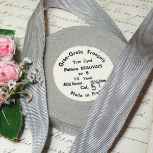 May include: A spool of gray grosgrain ribbon with the text "Gros-Grain Français" and "Pattern BEAUVAIS". The label indicates 10 yards of ribbon, 44% rayon, and 56% cotton. A length of ribbon is unspooled.