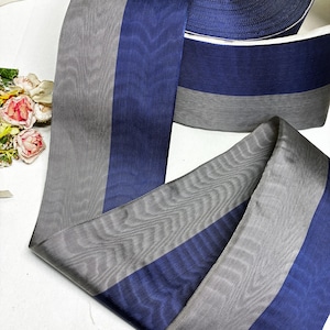 May include: A roll of navy blue and gray striped ribbon. The ribbon is made of a sheer material and is partially unrolled, revealing the texture and color variations. The ribbon is likely used for crafts, sewing, or gift wrapping.