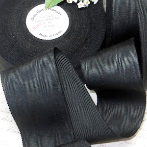 May include: Black grosgrain ribbon with a textured weave. The ribbon is 1 inch wide and comes in a 25 yard spool. The label reads "Gros Grain Francais, Yarn Dyed, Pattern BEAUVAIS, 1 in, 16, 25 Yards, Made in France".