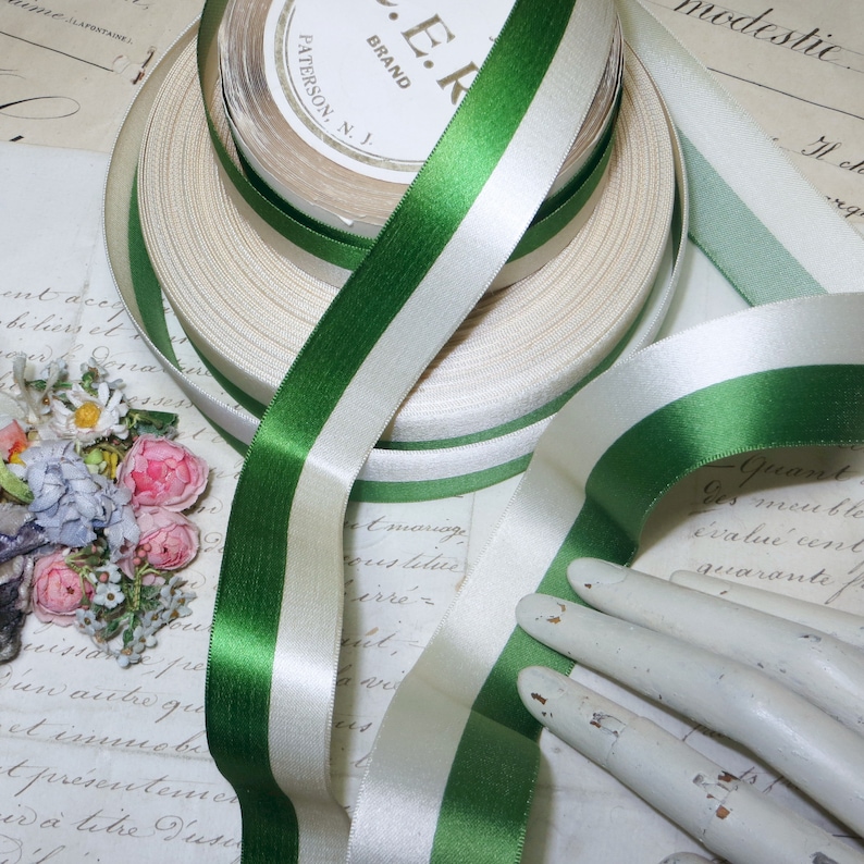 May include: Spools of satin ribbon in cream, white, and green. The ribbon is two-toned with a green stripe on each side of a white stripe. The ribbon is labeled "E.R. BRAND PATERSON, N.J."