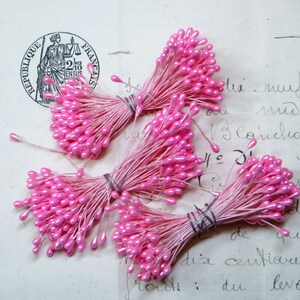 May include: Four bundles of pink flower stamens with small teardrop-shaped heads. The stamens are tied together with a thin wire.
