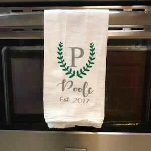 以下が含まれることがあります： 緑色の輪のデザインと中央に「P」の文字が書かれた白いキッチンタオル。輪の下に「Poole Est 2017」という文字が印刷されています。