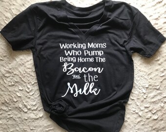 May include: Black v-neck t-shirt with white text that reads "Working Moms Who Pump Bring Home The Bacon and the Milk"