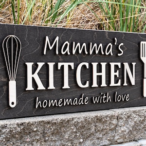 May include: A dark brown wooden sign with the text "Mamma's KITCHEN homemade with love" in white lettering. The sign also features a white silhouette of a whisk and a spatula.