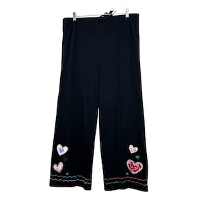 May include: Black wide-leg pants featuring an elastic drawstring waistband. The lower legs are decorated with embroidered heart motifs in red, white, and purple, accented by small green and blue hearts and wavy horizontal lines at the hem.