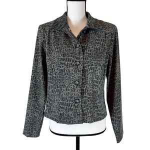 May include: A grey and black patterned button-down blazer. The long-sleeved jacket has a reptile-like design, a collared neckline, and three buttons. The blazer is displayed on a mannequin.