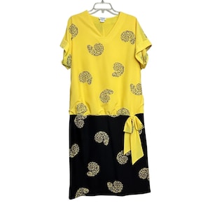 May include: A yellow and black dress with a V-neck and short sleeves. The top half is yellow with black spiral patterns, and the bottom half is black with matching spiral patterns. A yellow bow detail is on the side.