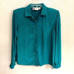 Può includere: Una camicia a maniche lunghe abbottonata di colore blu turchese con colletto. La camicia ha un'etichetta piccola che dice "Prophecy".