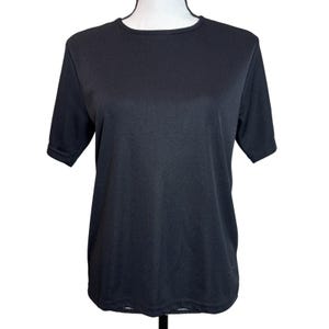 May include: A black short-sleeve t-shirt displayed on a mannequin. The shirt has a crew neck and a simple, classic design. The fabric appears to be a smooth, solid color, suitable for casual wear.