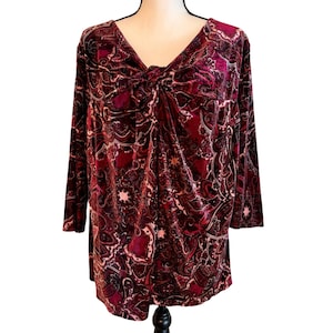 May include: A burgundy velvet top with a V-neck and long sleeves. The top features a knot detail at the bust and a paisley pattern in shades of burgundy, pink, and cream. The sleeves are three-quarter length.