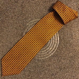 May include: A yellow and black patterned necktie with a woven design. The tie is folded and laid on a textured surface.