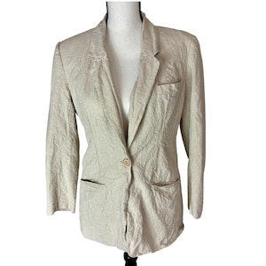 May include: A light beige blazer with a single-button closure, two front pockets, and a chest pocket. The blazer has a textured appearance and is displayed on a mannequin. The sleeves are three-quarter length.