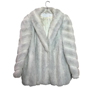 May include: A long-sleeved faux fur coat in a pale silver-grey color with a thick, wide collar and a smooth, light-colored interior lining. The coat features a vertical striped texture throughout the exterior and hangs on a clear hanger.