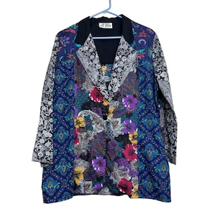 May include: A colorful blazer with a black collar and button closure. The jacket features a patchwork design with paisley, floral, and geometric patterns in shades of blue, purple, black, and white. The sleeves have a black and white floral pattern.