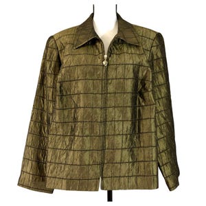 Puede incluir: Chaqueta verde oliva con cremallera y estampado de rejilla. La chaqueta tiene cuello y mangas largas. El tirador de la cremallera es un adorno decorativo plateado. La tela tiene un brillo sutil.