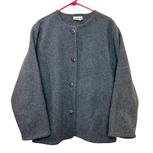 May include: A charcoal gray long-sleeved jacket made of a felted wool-like material. The jacket features a round neckline, a straight hem, and a front button closure with four dark metallic buttons. A small white brand label is visible at the neck.