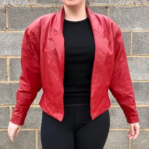 Puede incluir: Una chaqueta de cuero roja con cuello y cierre de botones. La chaqueta tiene una silueta ajustada y una longitud ligeramente recortada.