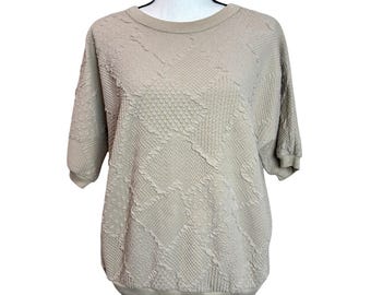 May include: A tan-colored short-sleeved sweatshirt with a textured, quilted pattern. The crew neck and sleeves have a ribbed design. The shirt is displayed on a mannequin.