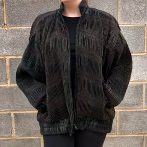 May include: A black, zippered jacket with a textured, striped pattern. The jacket has a stand-up collar and two pockets.