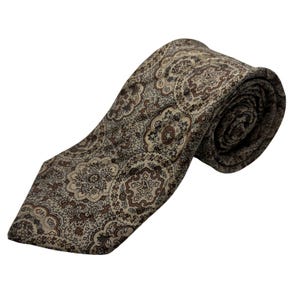 Puede incluir: Una corbata estampada en tonos marrón, beige y crema. La corbata presenta un diseño floral repetido. La corbata está enrollada en el extremo, mostrando la textura y el patrón de la tela. La corbata está sobre un fondo blanco.