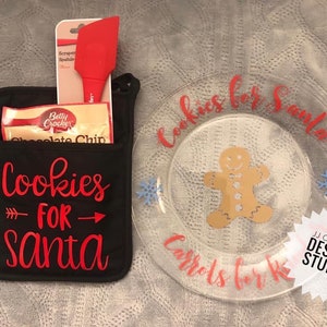 Pode incluir: Uma luva de forno preta com o texto "Cookies for Santa" em vermelho, segurando uma espátula vermelha e um pacote de mistura para biscoitos com pepitas de chocolate. Um prato transparente com "Cookies for Santa" e "Carrots for Reindeer" em vermelho, além de um boneco de gengibre.