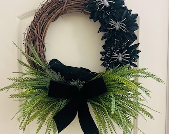 May include: A Halloween wreath with a grapevine base, adorned with black flowers, glittery spiders, and a black crow. Greenery and a black velvet bow complete the festive design. This decorative wreath is perfect for seasonal home decor.