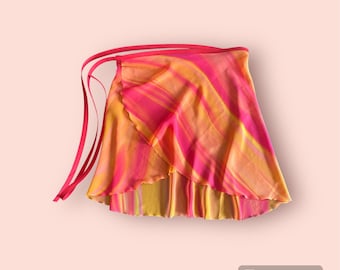 May include: A vibrant wrap skirt in shades of pink, orange, and yellow, featuring a flowing, layered design. The skirt has long, matching pink ties for securing around the waist. The fabric has a swirled pattern.