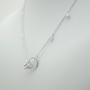 May include: A silver necklace with a double circle pendant. The pendant features Roman numerals around one circle and a row of clear cubic zirconia stones around the other circle. The necklace also has two smaller clear cubic zirconia stones hanging from the chain.