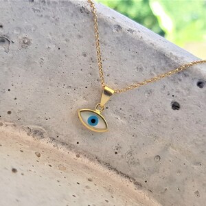 May include: A gold chain necklace with a blue and white evil eye pendant. The pendant is a small, oval-shaped charm with a blue eye in the center.