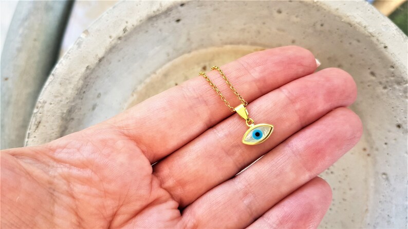 May include: Gold chain necklace with a small blue evil eye pendant.