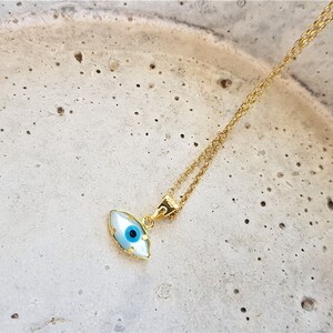 May include: A gold chain necklace with a blue and white evil eye pendant. The pendant is shaped like an eye and has a gold rim.