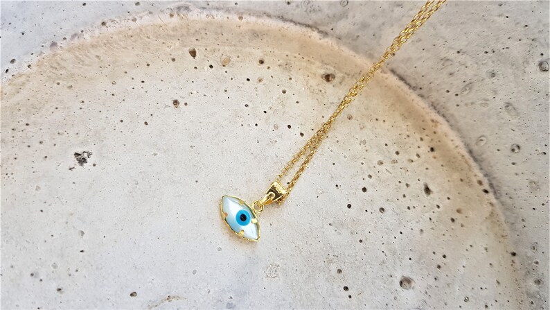May include: A gold chain necklace with a blue and white evil eye pendant. The pendant is shaped like an eye and has a gold rim.