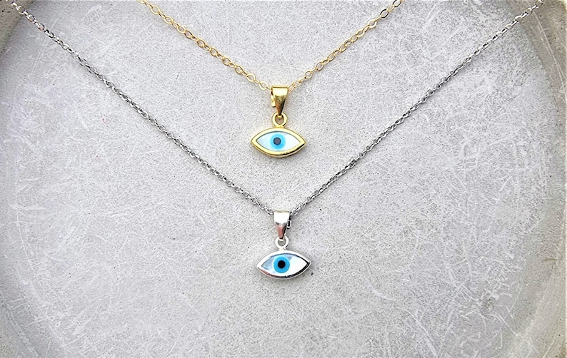 May include: Two silver necklaces with blue evil eye pendants. The top necklace has a gold chain and the bottom necklace has a silver chain.
